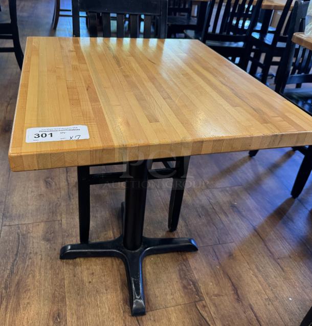 Wooden dining table with square butcher block top and black metal base. Auction tag indicates bid number 301, quantity 7.