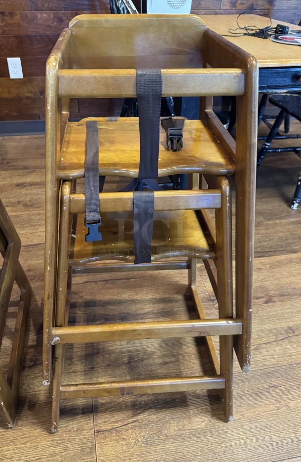 Wooden high chair for children, features safety strap, visible wear on edges, sturdy design, rectangular frame.