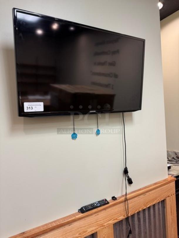 Samsung 42" TV mounted on wall, includes remote control. Tested and working. Auction tag visible.