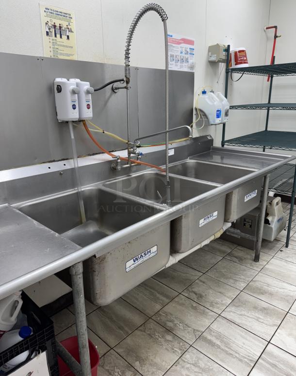 3 compartment sink with drainboards and pre-rinse faucet, stainless steel, labeled "Wash," "Rinse," "Sanitize," in used condition.