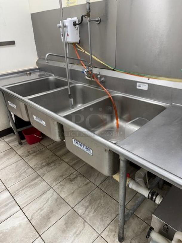 Three-compartment stainless steel sink with drainboards, pre-rinse faucet, Ideal for commercial kitchens, good condition.