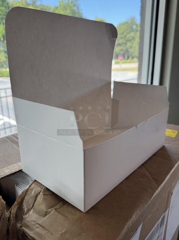 New small white disposable bakery box, open lid, pristine condition, plain design, on a cardboard case.
