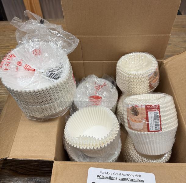 Jumbo cupcake liners in open box, multiple packs, labeled "Capri 130 pcs". New condition, white color.