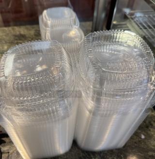 Clear plastic take-out containers stacked. Square shape, hinged lids. Suitable for food storage. Good condition.