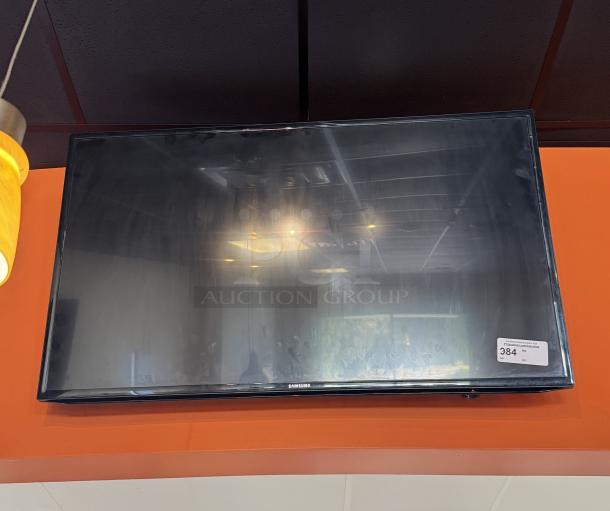 Samsung 52" TV mounted on wall, with remote. Tested and working, includes a visible auction label with number 384.