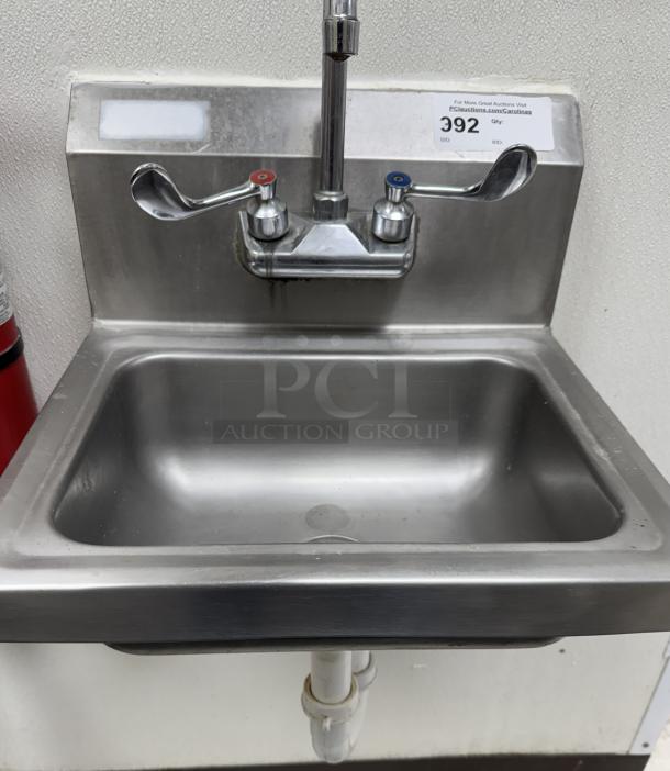 Stainless steel wall mount hand wash sink with dual-handle faucet, auction tag showing lot number 392, used condition.