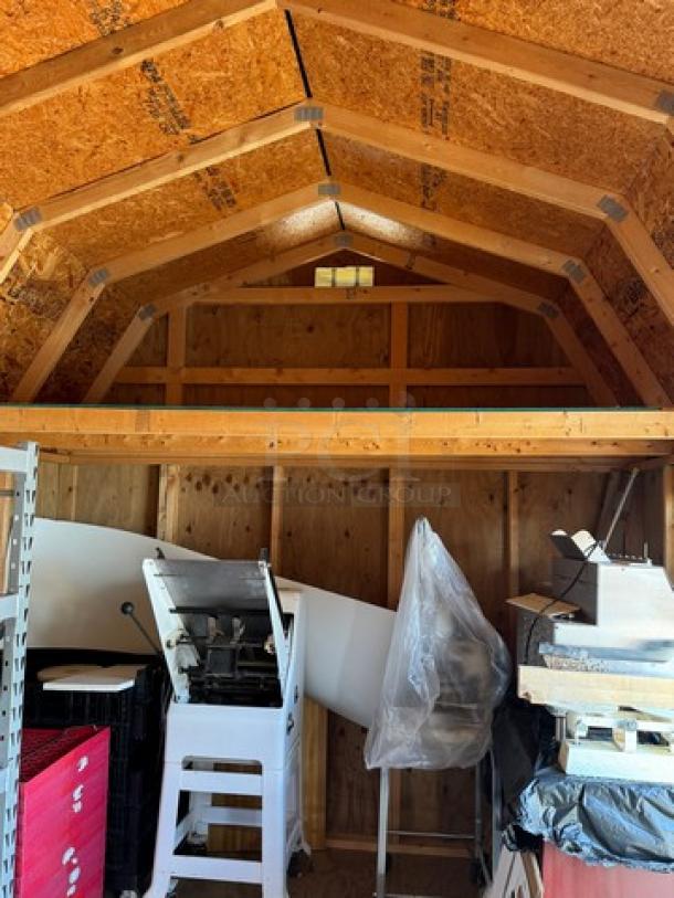 Wood barn interior with a metal roof, featuring exposed wooden beams and a loft. Contains stacked items and machinery.