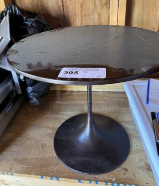 Round metal table with a simple pedestal base. Visible light wear on the surface. Auction tag "395" attached.