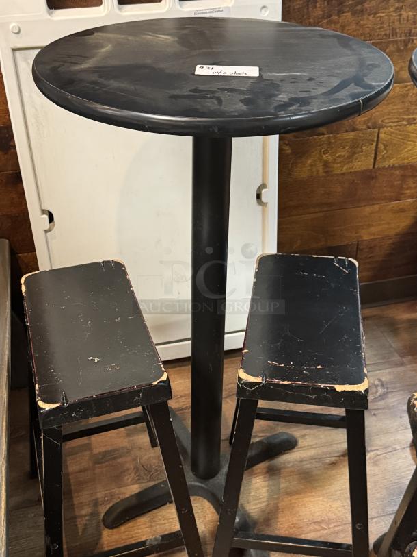 Black round bar height table with two matching stools, showing signs of wear on edges. 