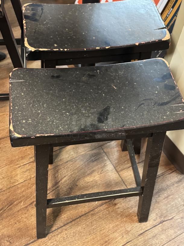 Two worn, black stools with scuffed surfaces and visible edge wear, part of a set with a black round table.