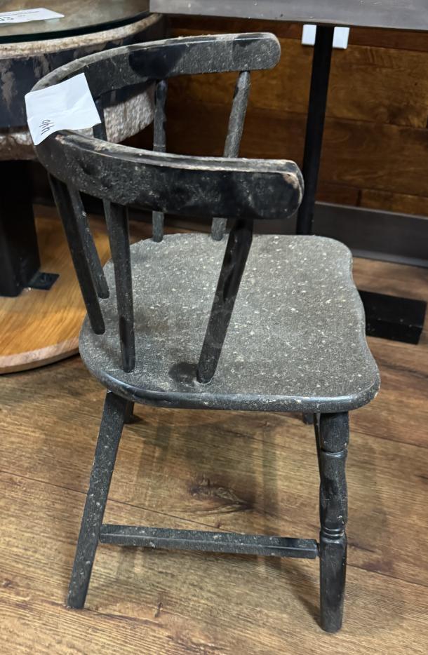 Black child's chair with curved back, sturdy design, worn condition. Visible tag with number 999; suitable for vintage decor.