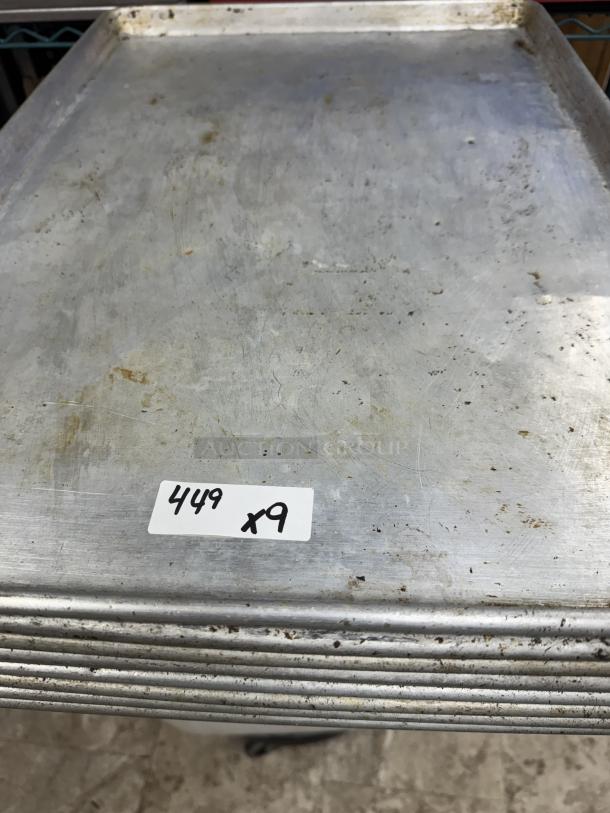 Full size sheet pans stack, moderate wear, labeled "449 x9," metal construction, suitable for commercial baking.