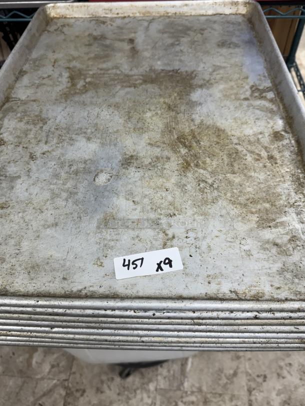 Nine full-size sheet pans, used, stacked together with visible wear. A tag reads "457 x9."