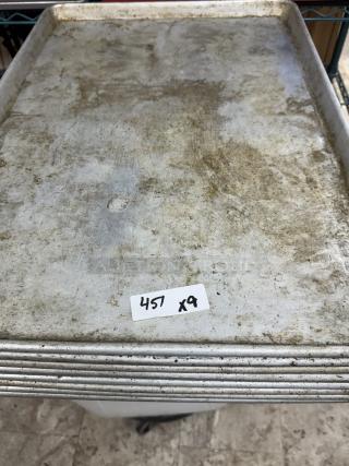 Nine full-size sheet pans, used, stacked together with visible wear. A tag reads "457 x9."