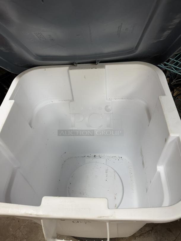 Rubbermaid 28 Gal. dry storage container, white interior with open lid, some signs of use, includes dollie for mobility.