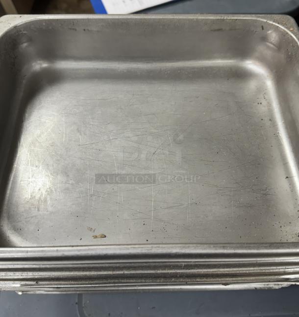Stainless steel half pans, visible wear, stack of nine. Scratches and minor stains indicating used condition.
