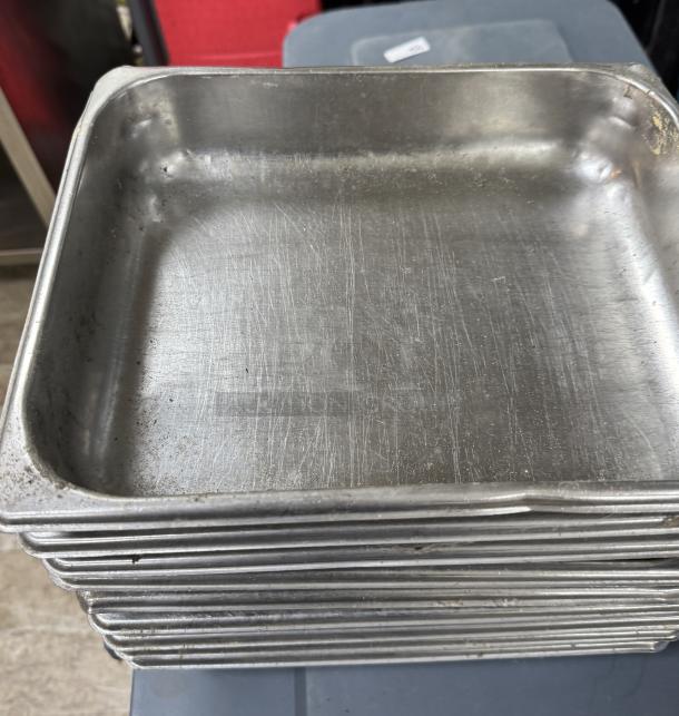 Stack of nine stainless steel half pans, used condition, visible surface scratches and slight wear, suitable for catering.