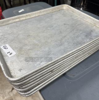 Nine half-size sheet pans, stacked, metal, signs of wear, auction label visible, suitable for baking or roasting.