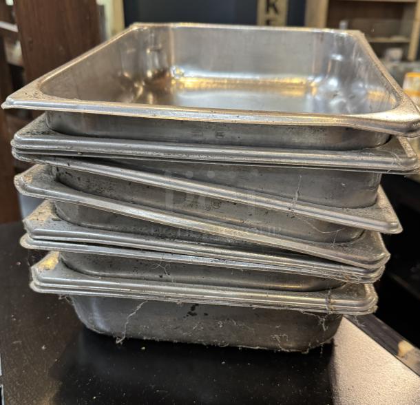 Stack of nine stainless steel half-size sheet pans in used condition, visible wear and scratches, PIN 20229 engraved.