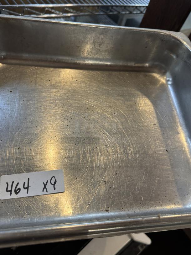 Stainless steel half size sheet pan, showing signs of use with surface scratches. Label reads "464 x9."