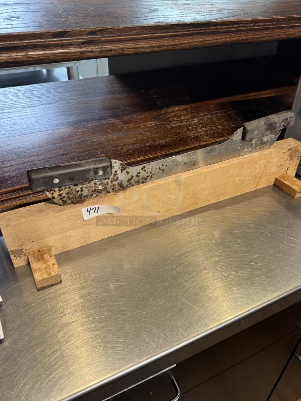 Dough cutter on stand, metal blade with black handle, wooden base, labeled "471." Evidence of rust on the blade.