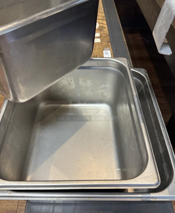 Assorted Vollrath and Update stainless pans in various sizes, stacked, showing minor wear. Ideal for kitchen use.