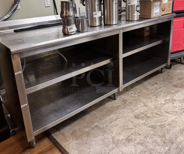 Large stainless steel table with open storage shelves, used condition. Features two compartments and visible wear marks.