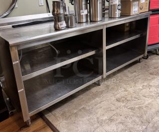 Large stainless steel table with open storage shelves, used condition. Features two compartments and visible wear marks.