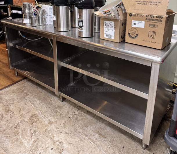 Large stainless steel table with open storage, dual shelves, clean surface, minor wear. Ideal for commercial use.