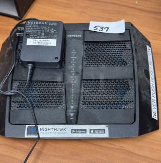 Netgear Nighthawk router model 4MRA8770A1FBB with power adapter, showing status lights and "537" label.