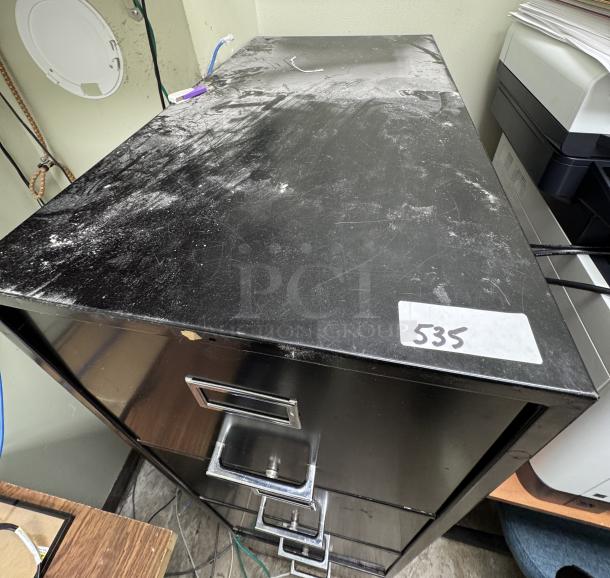 Black 4 drawer filing cabinet, used condition, visible dust and wear on top surface, number "535" label attached.