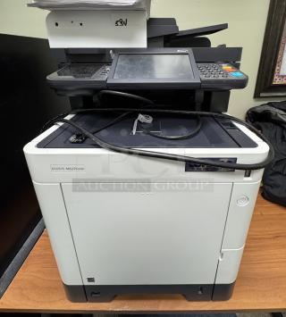 Ecosys M6235cidn printer on desk with assorted paper on top, touchscreen interface, cables, visible label indicates model and brand.