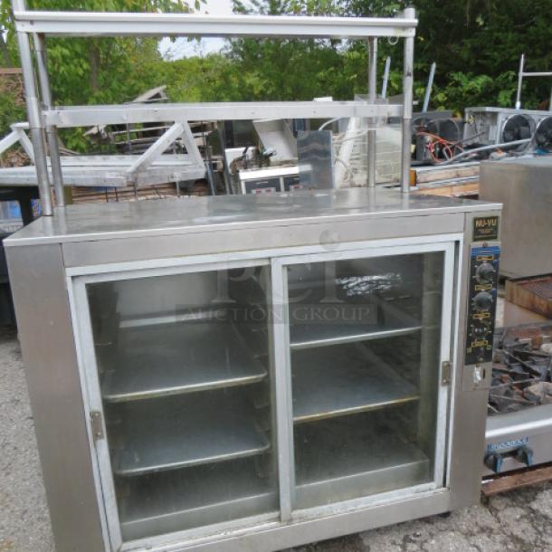 NUVU heated holding cabinet with two glass sliding doors, two stainless steel shelves, casters, tags showing controls, 48x31x64 inches.