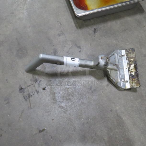 Metal griddle scraper with angled handle, showing signs of wear, label attached with the number "0".