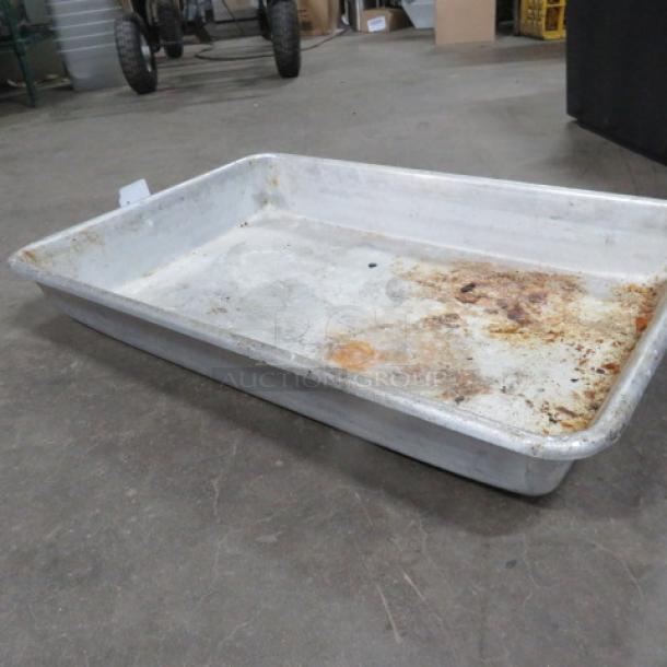 Worn aluminum roasting pan on concrete floor, showing signs of use with discoloration and residue. No visible markings.