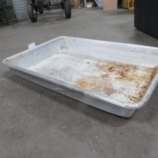 Worn aluminum roasting pan on concrete floor, showing signs of use with discoloration and residue. No visible markings.