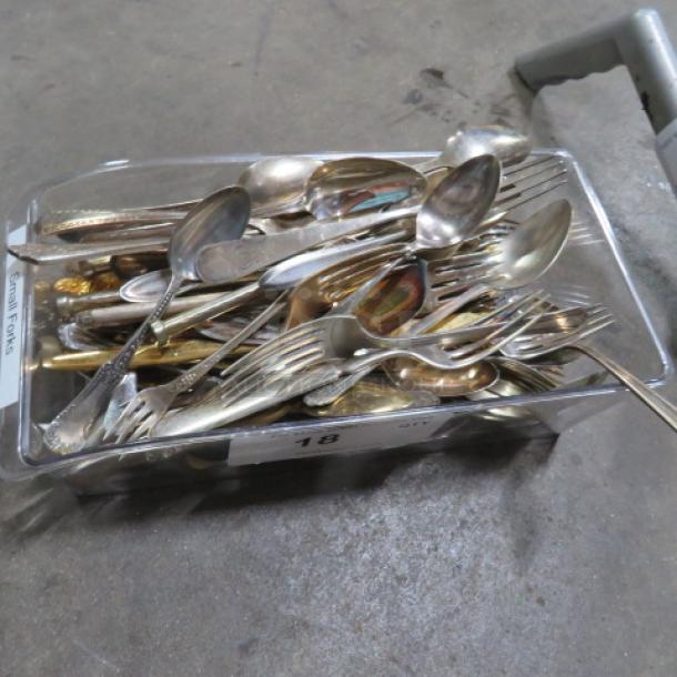A clear container filled with assorted flatware, including forks, spoons, and knives in various metals and styles.