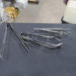 Assorted stainless steel tongs, various types and sizes, in good condition on a black table.