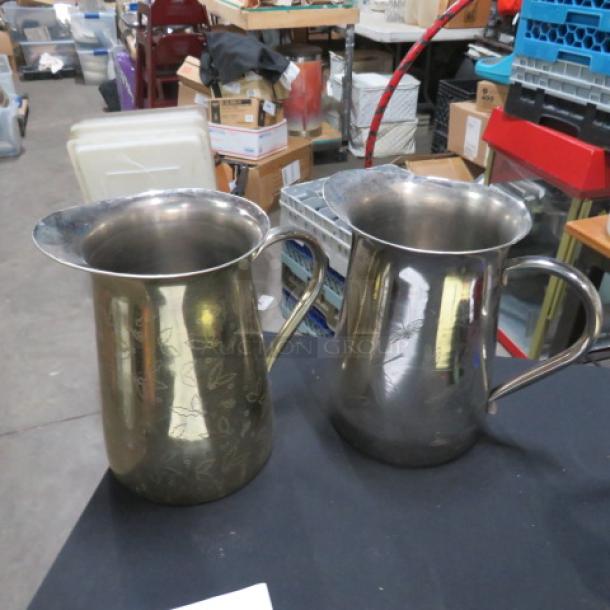 Two stainless steel water pitchers, slightly tarnished, with engraved floral patterns and large handles. Model 2XBID.
