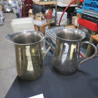 Two stainless steel water pitchers, slightly tarnished, with engraved floral patterns and large handles. Model 2XBID.