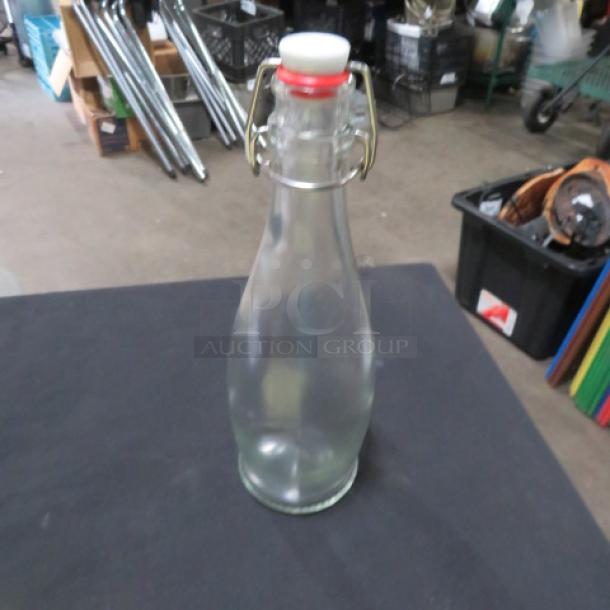 Clear glass water bottle with hinged lid, red and white cap. Model 7XBID. In good condition. Ideal for kitchen use.