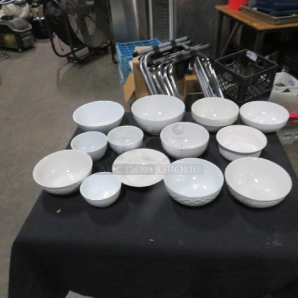 Lot of 13 assorted size white bowls on display table, varying designs and conditions, featuring smooth and textured surfaces.
