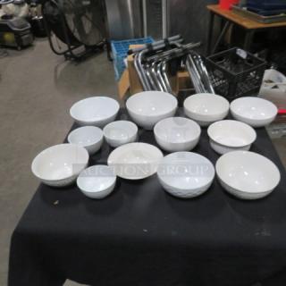 Lot of 13 assorted size white bowls on display table, varying designs and conditions, featuring smooth and textured surfaces.