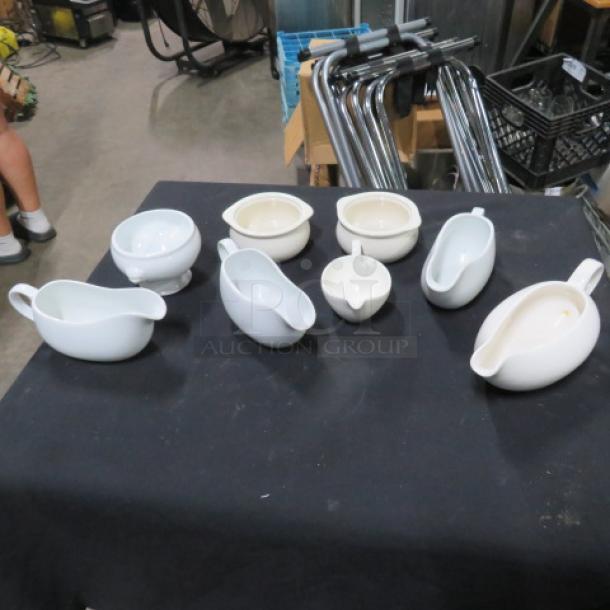 Assorted gravy boats and sugar bowls, set of 8, in various white porcelains, placed on a black tablecloth.