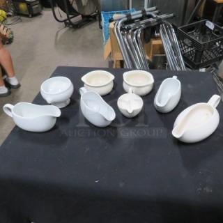 Assorted gravy boats and sugar bowls, set of 8, in various white porcelains, placed on a black tablecloth.