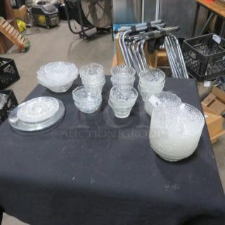 Assorted glassware lot featuring bowls and plates displayed on a table. Clear glass with textured and etched designs.