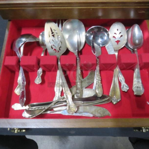 Wooden flatware box with one drawer, containing assorted vintage flatware on a red felt interior.