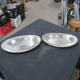 Two silver serving platters, 12.5x7.5 inches, featuring beaded edges, in good condition on a black table.