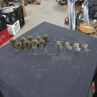 One lot of 13 assorted silver plate napkin rings on a table; round and square designs visible, good condition.