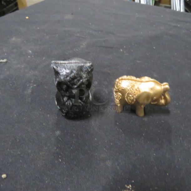 One black owl and one gold elephant place card holder on a black surface.